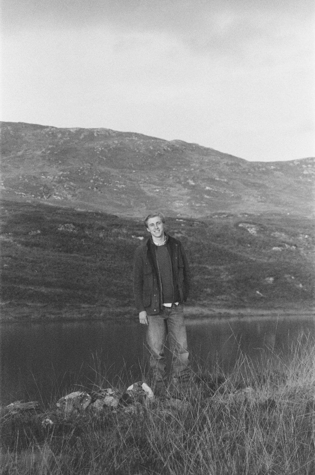 Nikolaus Niewerth standing by a lake in the hills, black-and-white film photograph